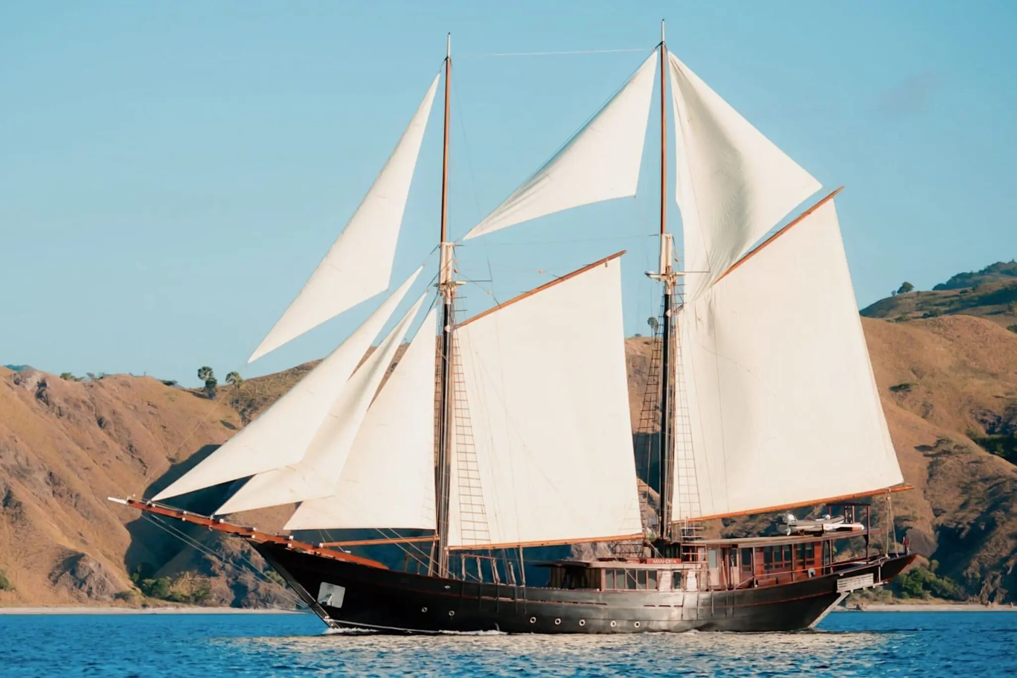 Amandira luxury phinisi yacht sailing through turquoise waters in Indonesia, surrounded by tropical islands